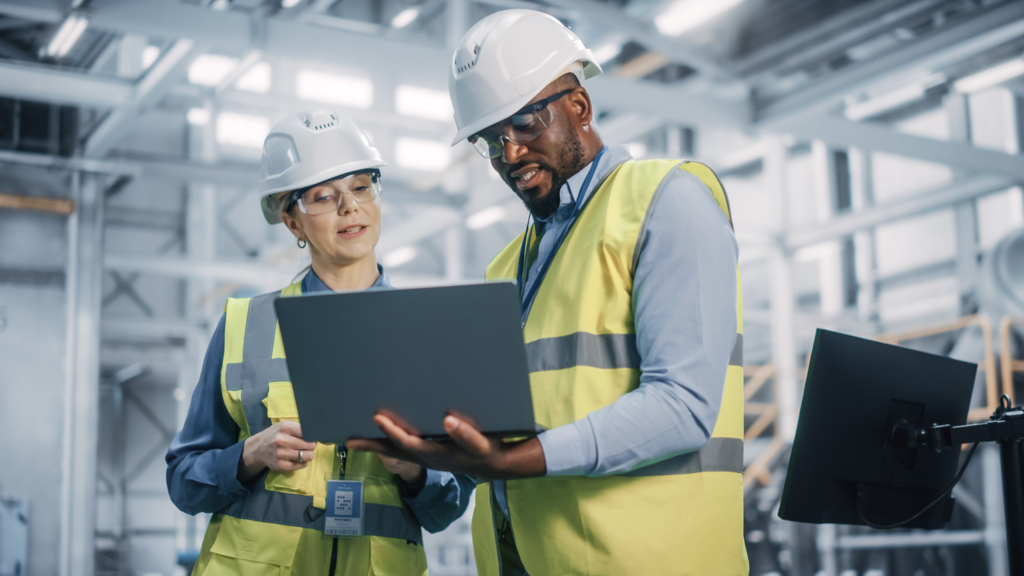 Employees analyze a laptop in a factory to monitor their assets with eam cmms.